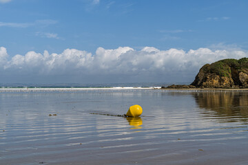 Bou&eacute;e jaune &eacute;chou&eacute;e sur le sable &agrave; mar&eacute;e basse, reflet dans l&rsquo;eau et nuages sur une plage bretonne.