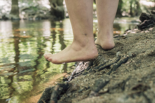 Woman with lipedema entering river in forest, testing water with foot