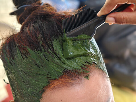 Close up of woman dyeing hair with natural green henna herbal paste