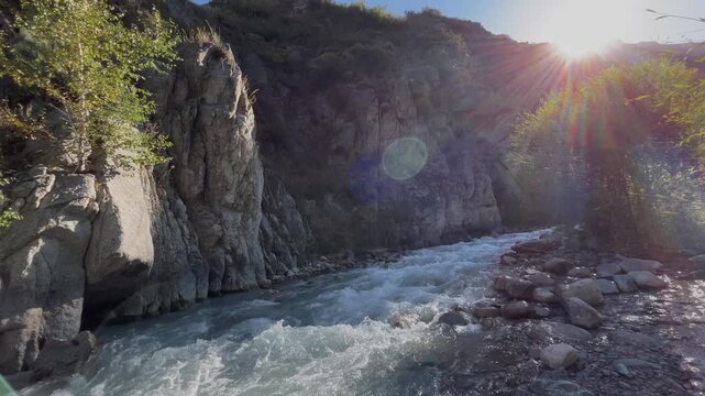 Beautiful landscape with a mountain river flowing among rocky cliffs. Sunlight shines in the background, creating a scenic wilderness view with natural water stream, rugged terrain, and peaceful outdo