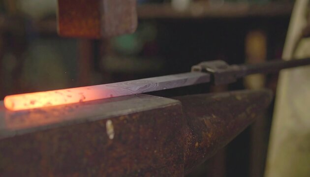 Glowing metal rod hammered on anvil in workshop
