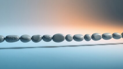 A string of gray beads of varying sizes on a thin wire against a gradient background of blue and orange
