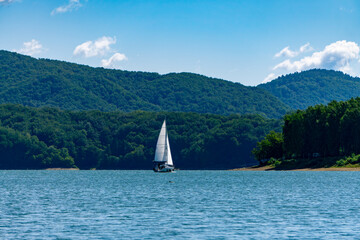 Solina Lake with a sailing boat against green Bieszczady mountains, calm water, summer scenic view.