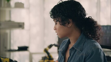 Focused female engineer working in modern office with robotic arm and computer, symbolizing artificial intelligence, innovation, and STEM research.