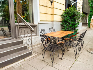 Wooden table with decorative metal chairs on cafe terrace beside window and stone stairs. Outdoor dining, hospitality, lifestyle, architecture and urban street culture.