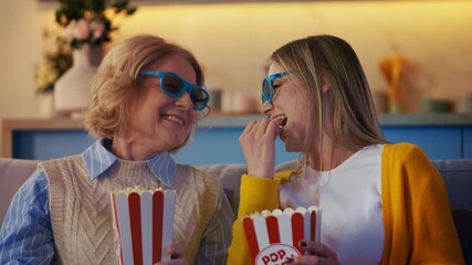 Happy senior woman and daughter watching movie together and eating popcorn - Powered by Adobe
