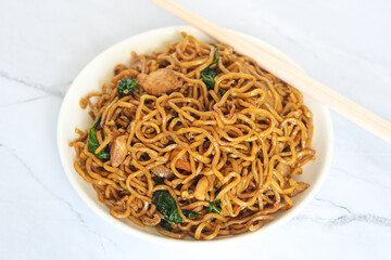 Top view of delicious fried noodles with savory sauce, vegetables, and meat. Next to it are chopsticks. Captured with natural light and a marble background.