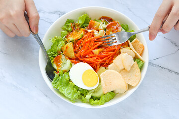 Person eating Rujak Pengantin, an Indonesian salad featuring fresh lettuce, cucumber, shredded carrot, hard-boiled egg, kerupuk (crackers), boiled potato, cabbage, and coated in a rich peanut sauce.