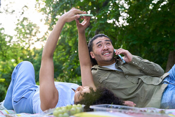 Couple lying on picnic blanket using smartphones in park