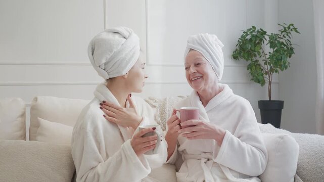 Senior woman and adult daughter in bathrobes drinking tea after spa treatments