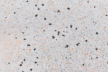 Detailed close-up of terrazzo texture with randomly scattered small fragments in gray, black, orange, and white on a light background.