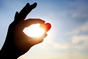 A silhouette of a woman holding a red heart, a symbol of precious life and love, against a blue sky...