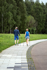 woman and man training with walking poles in park. back view against a trees background