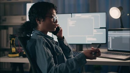 Software engineer woman wearing glasses talking on smartphone while coding robotics and artificial intelligence late at night, focusing on cybersecurity and data research in a modern high-tech office. - Powered by Adobe