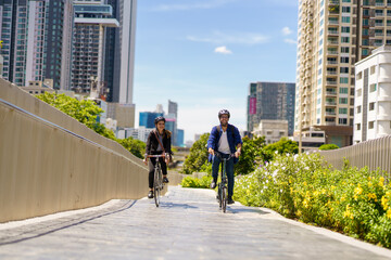 Asian man with female friend cycling, commuting to work for health and eco lifestyle.