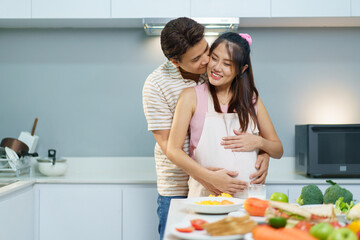 Asian couple with pregnant wife cooking breakfast in kitchen. Warm family love, bonding, and lifestyle at home.