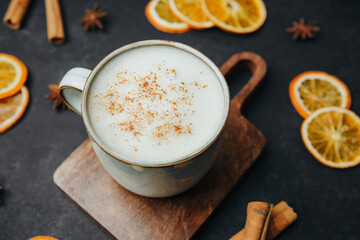 Hot creamy drink with cinnamon sprinkled on top, served with dried orange slices and cinnamon sticks.