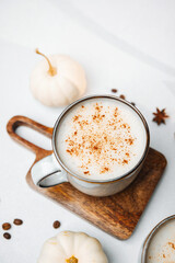 Warm creamy coffee drink dusted with cinnamon on a wooden board with mini white pumpkins and coffee beans.