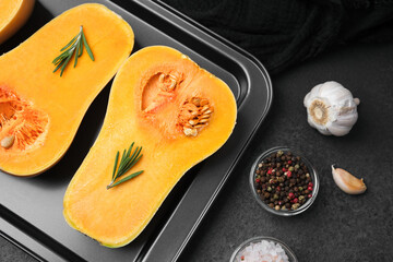 Butternut squash halves with rosemary on baking tray with garlic and peppercorns