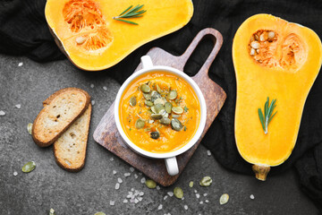 Golden squash soup with seeds and bread on a dark surface, healthy meal
