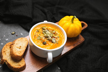 Hearty pumpkin soup topped with seeds, served with crispy bread slices and a small decorative gourd.