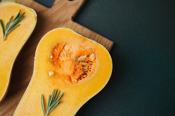 Butternut squash halves with fresh rosemary sprigs on a rustic wooden board.