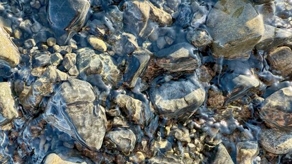 smooth river stones under clear flowing water with shimmering sunlight reflections perfect for natural background or calming texture
