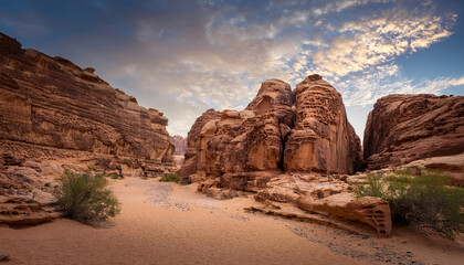 discovering dramatic ancient stone structures within a vast rugged desert canyon filled with stunning natural rock formations against a cloudy sky