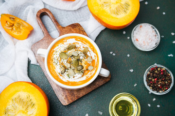 Creamy pumpkin soup with seeds and herbs served in a bowl with fresh pumpkin slices and spices