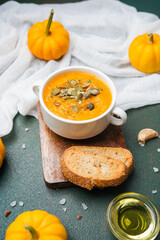 Bowl of orange soup topped with seeds, served with toasted bread and small pumpkins on a dark surface.