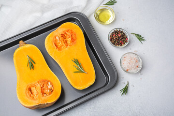 Halved butternut squash with rosemary seasoning on baking tray ready for cooking with salt and pepper.