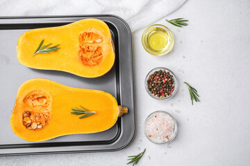 Butternut squash halves on baking sheet with rosemary, oil, salt, and peppercorns.