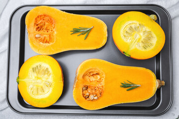 Halved butternut squash and round squash with rosemary on baking tray for cooking preparation