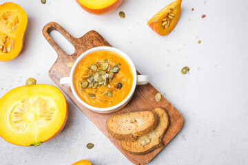 Bowl of pumpkin soup with pumpkin seeds and toast on wooden board, surrounded by pumpkins
