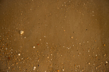 Wet sand texture featuring small stones and pebbles forms a stunning natural pattern, ideal for creating backgrounds and textures that evoke the beauty of the seaside