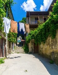 Sunny alleyway with clothes strung between weathered stone buildings and a stairway.
