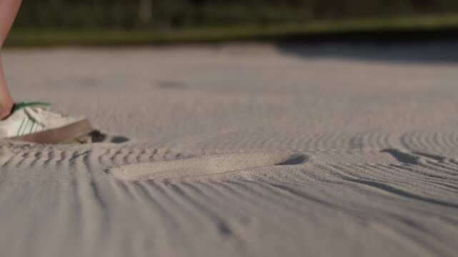 Woman golfer executes shot launching golf ball from sandy bunker