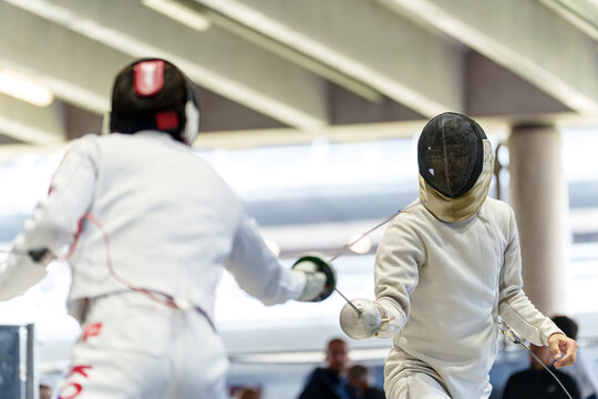 Two athletes in protective gear competing in a fencing match with epee swords