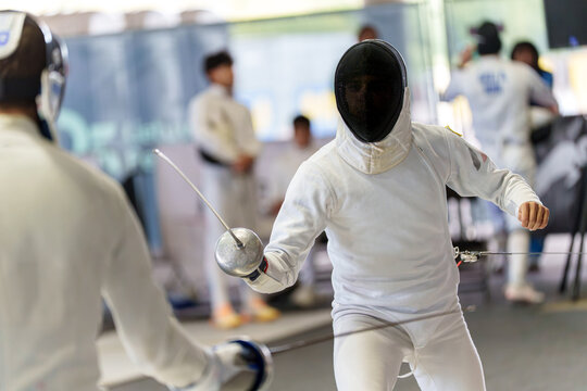 Fencers in protective gear competing fencing in a duel with swords during match