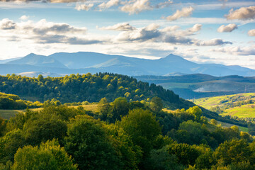 countryside landscape of transcarpathia on september evening. village in the valley and rural fields on the forested hills. carpathian mountain ridge with pikui peak in the distance
