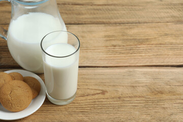 Glass of milk with jug and cookies on table
