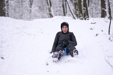 Woman enjoying sledding down snowy hill in winter forest