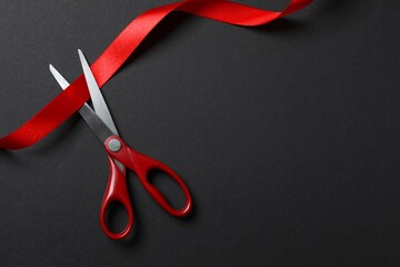 Beautiful red ribbon and scissors on black background, flat lay with space for text. Ceremonial tape cutting