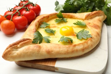 Tasty khachapuri with cheese, egg, parsley and tomatoes on white table, closeup