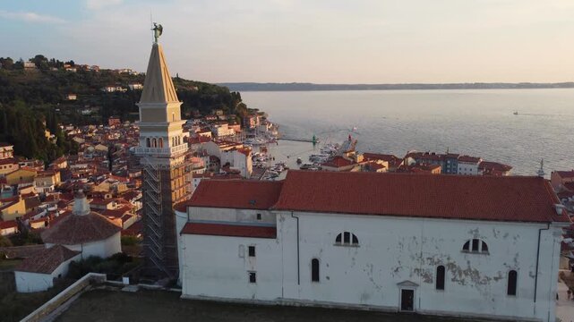 Aerial view of the Church of St. George with the tourist town of Piran in the background. Drone view of the church and bell tower in the old coastal town in Slovenia at sunset