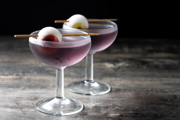 Purple Halloween cocktail garnished with candy eye on wooden table and dark background. Copy space