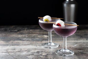 Purple Halloween cocktail garnished with candy eye on wooden table and dark background. Copy space