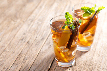 Refreshing peach iced tea in glass with ice cubes and cinnamon on wooden table. Copy space
