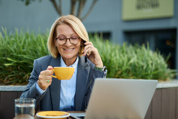 Portrait of a mid aged mature businesswoman using a laptop and drinking coffee in a coffee shop
