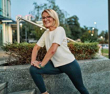 Portrait of a middle aged mature  beautiful sport woman smiling happy and confident. Standing and  doing exercise and stretching  in city park outdoors